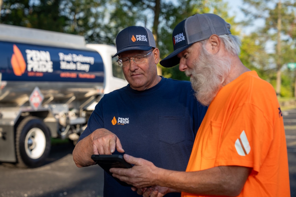 two employees reviewing an order on a tablet with a fuel truck in the background
