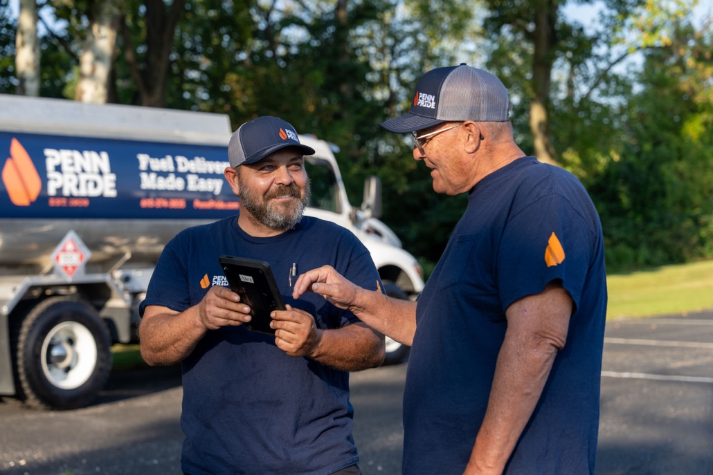 two employees reviewing order on a tablet with fuel truck in the background