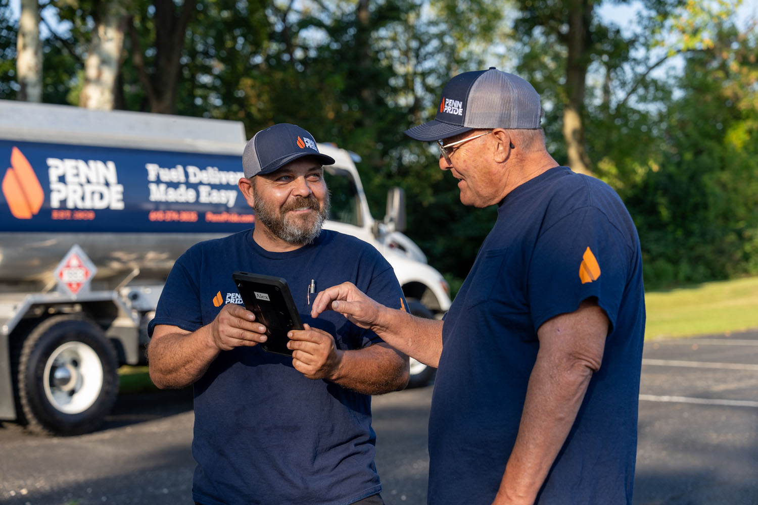 two employees reviewing order on a tablet with fuel truck in the background